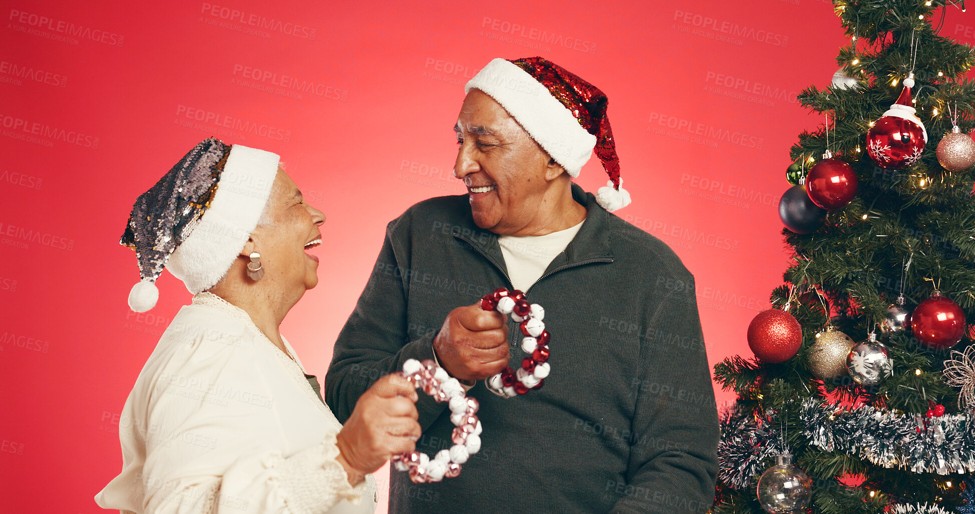 Buy stock photo Senior couple, christmas or tree with music in studio for festive celebration on a red background. Elderly, man and woman with smile or shaker for december holiday, santa or weekend surprise together