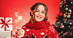 Portrait, Christmas and child with sparkler, studio and excited for celebration or December holiday. Red background, festive season and girl with Xmas sweater, presents and tree with ornaments in USA