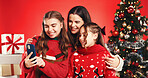 Christmas, mother and kids with selfie in studio for festive season, hug and bonding together. Happy family, people and photo on red background for xmas memory, holiday fashion and winter celebration