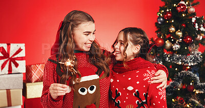 Buy stock photo Happy, sisters and children with sparkler, Christmas and bonding on festive season, hug and holiday. Studio, teenager and embrace with girl, family and love on Xmas, red background or decorations
