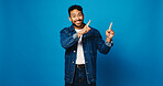 Portrait, pointing up and man in studio, smile and announcement with offer on blue background. Model, space and happy person with hand gesture, opinion and opportunity with decision or choice