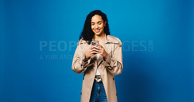 Buy stock photo Phone, smile and typing with woman in studio for connection, text message and social media. Online news feed, search and mockup space with person on blue background for post update and network