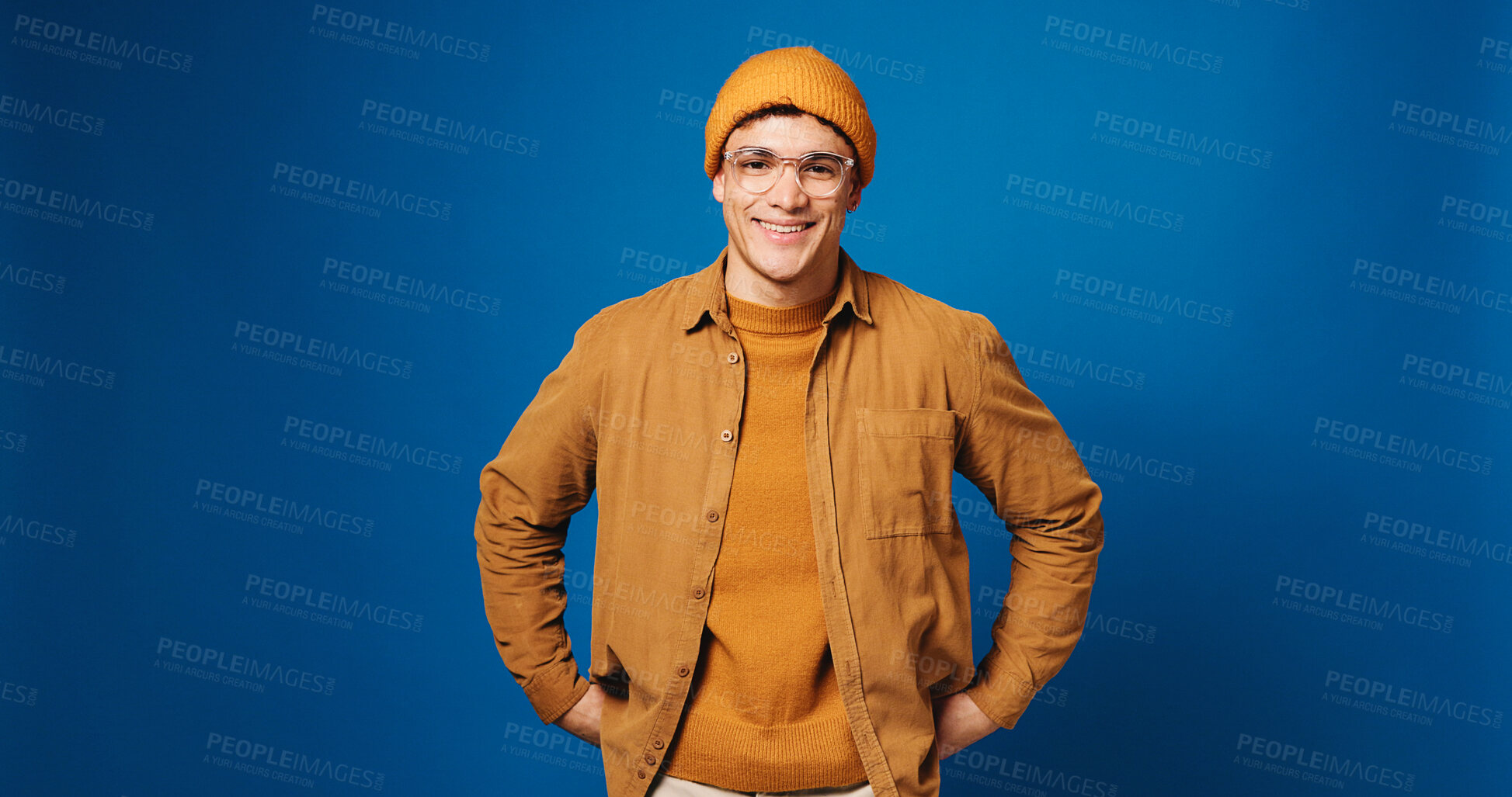 Buy stock photo Man, fashion and smile in studio portrait with beanie, glasses and trendy style on blue background. Person, happy and pride with confidence, edgy clothes and hat with mock up space in Costa Rica