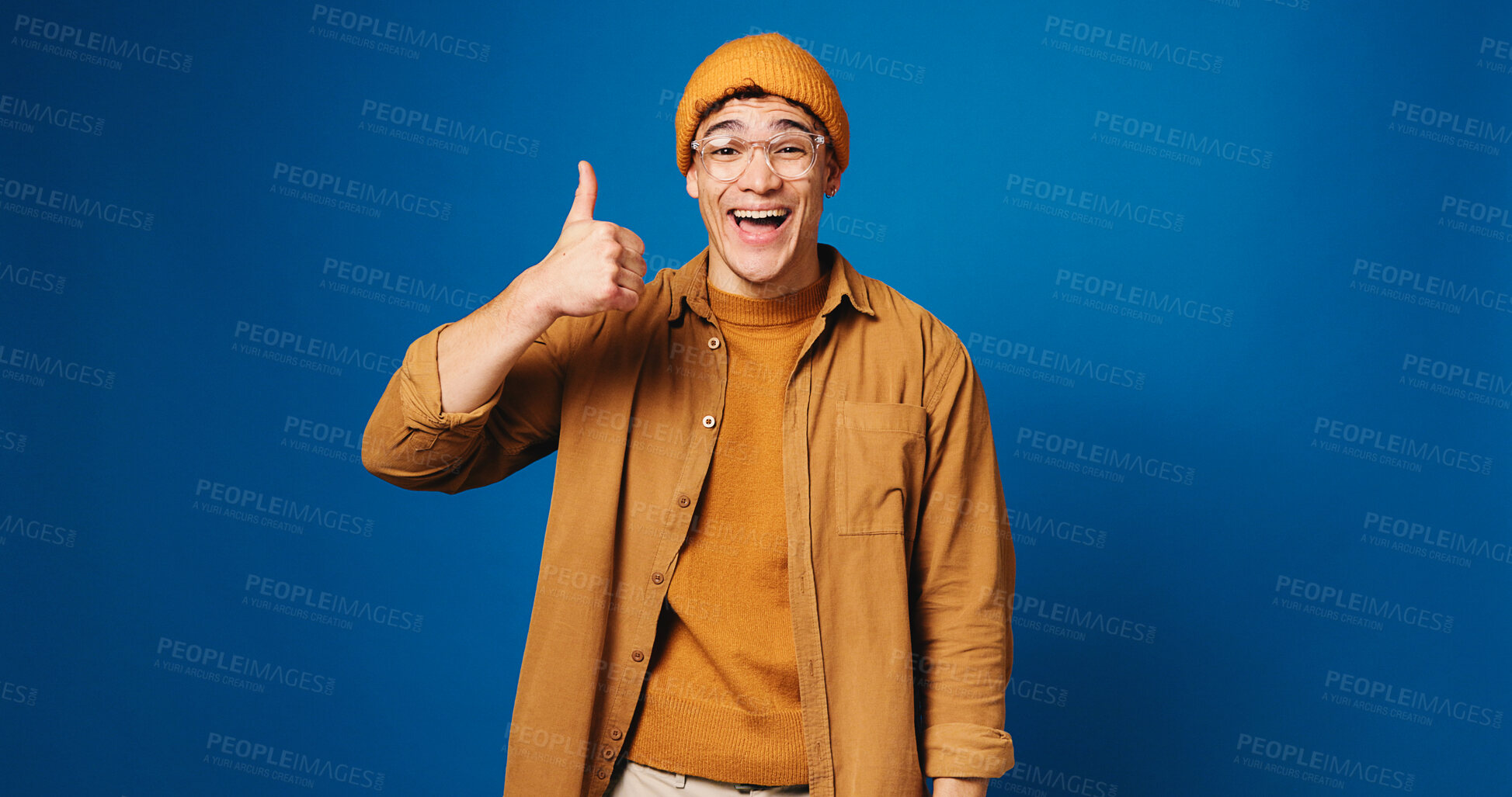 Buy stock photo Happy man, portrait and fashion with thumbs up in studio for good choice on a blue background. Male person, model or gen z with smile, like emoji or yes sign for style or clothing on mockup space