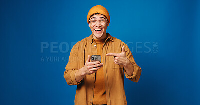 Buy stock photo Man, wow or pointing at phone in studio with news, notification or sale on blue background. Surprise, mobile or portrait of excited person with shock for discount, promo or giveaway with mockup space
