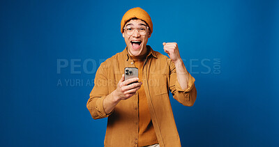 Buy stock photo Student, fist pump and phone with portrait of man in studio for surprise, scholarship award or winner. College acceptance, happy and mockup space with person on blue background for online application