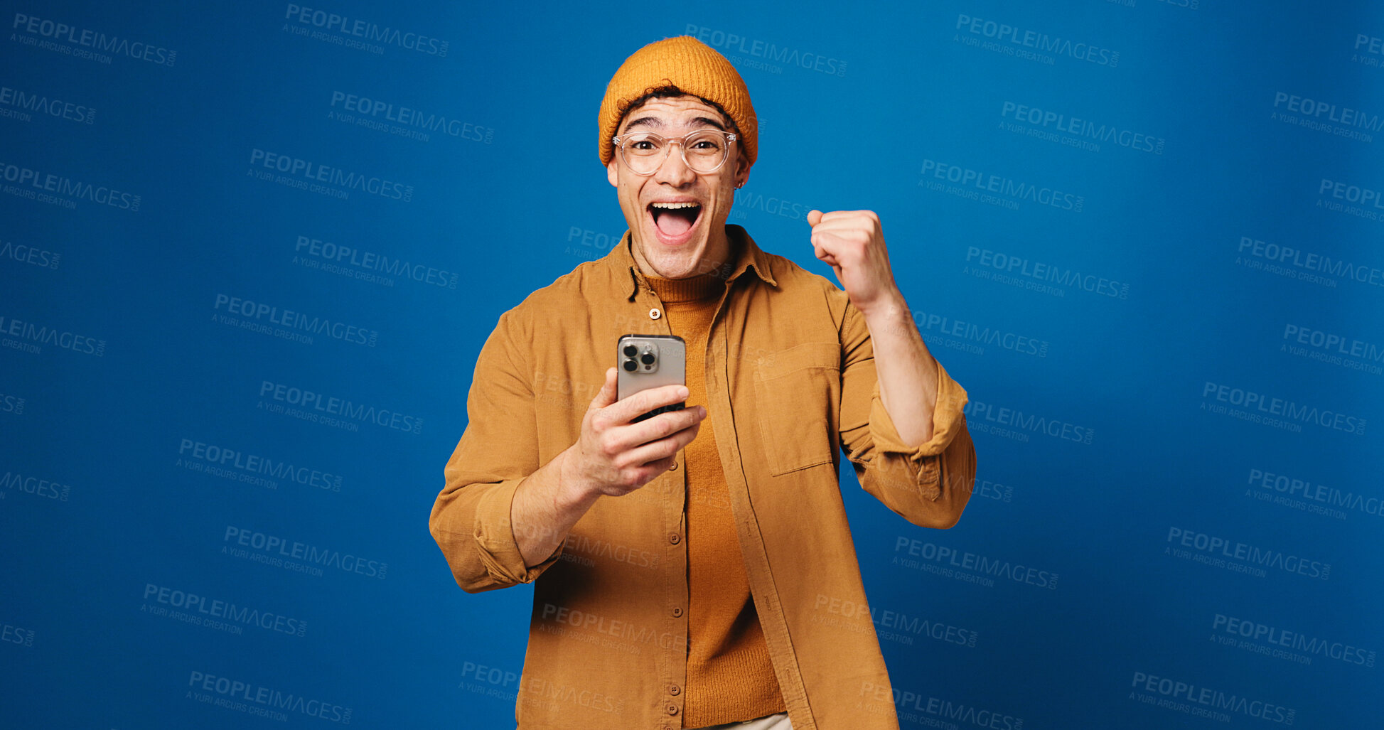 Buy stock photo Student, fist pump and phone with portrait of man in studio for surprise, scholarship award or winner. College acceptance, happy and mockup space with person on blue background for online application