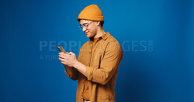 Buy stock photo Phone, happy and man in studio with networking, communication or texting on mobile app. Mockup space, technology and person with cellphone for chatting, contact or social media by blue background.