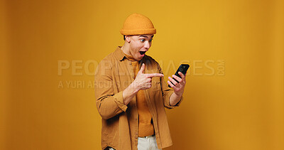 Buy stock photo Phone, excited and man in studio with good news, winning or giveaway prize on mobile app. Mockup space, pointing and person with cellphone for notification of gambling bonus by yellow background.