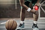 Sports injury, basketball and injured knee or athlete man while on an outdoors court holding his leg in pain during training or exercise for hobby. Closeup of male hands on glowing red body part