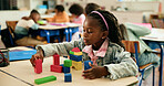 Girl, child and building with blocks in classroom, learning and puzzle with problem solving for education. Kid, wood toys and development with shapes, solution and thinking at elementary school