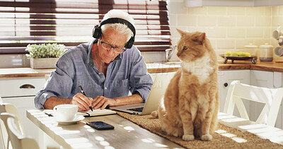 Buy stock photo Writing, headphones and old man in kitchen with cat, laptop and notebook for morning routine. Music, animal and person in house with coffee, technology and checklist for daily task planning.