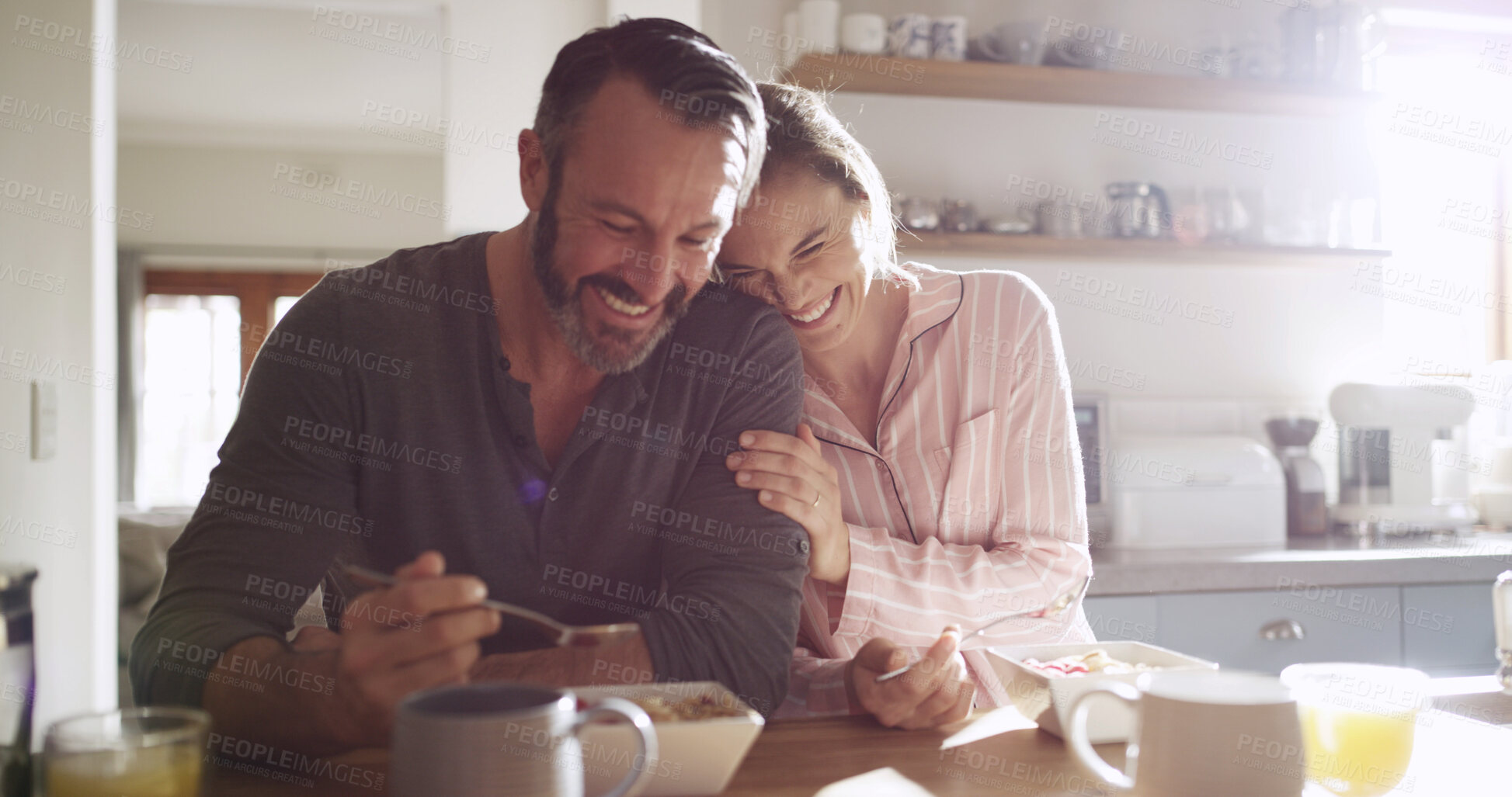 Buy stock photo Happy couple, laugh and eating breakfast in kitchen for health, nutrition and diet with partner. Funny, hungry man and woman with morning meal, cereal and enjoy food with embrace for love in home