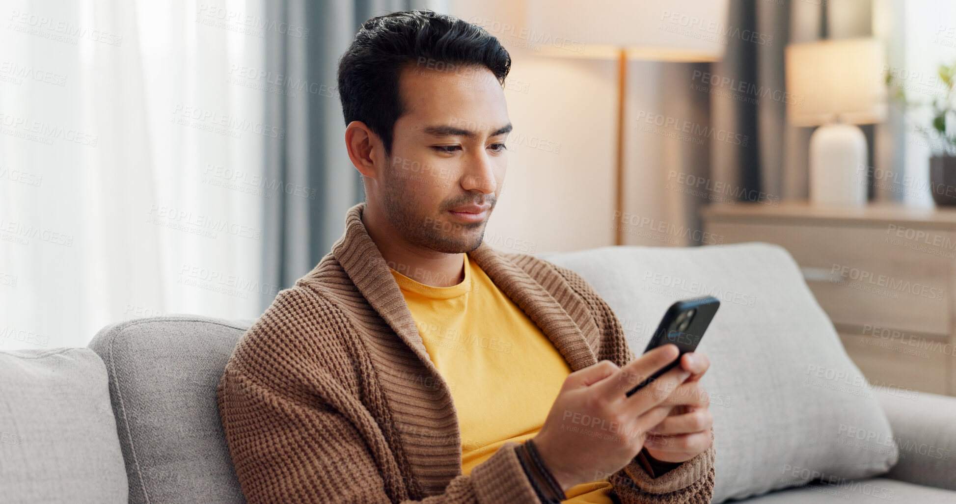 Buy stock photo Phone, relax and scrolling with man on sofa in living room of home for social media browsing. App, communication and reading with person typing in apartment for internet search or text message