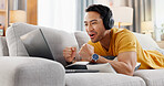 Man, laptop and headphones on sofa for sport, social media and video streaming or website in home. Excited, cheer and male person on couch with technology, break and watching tournament on app