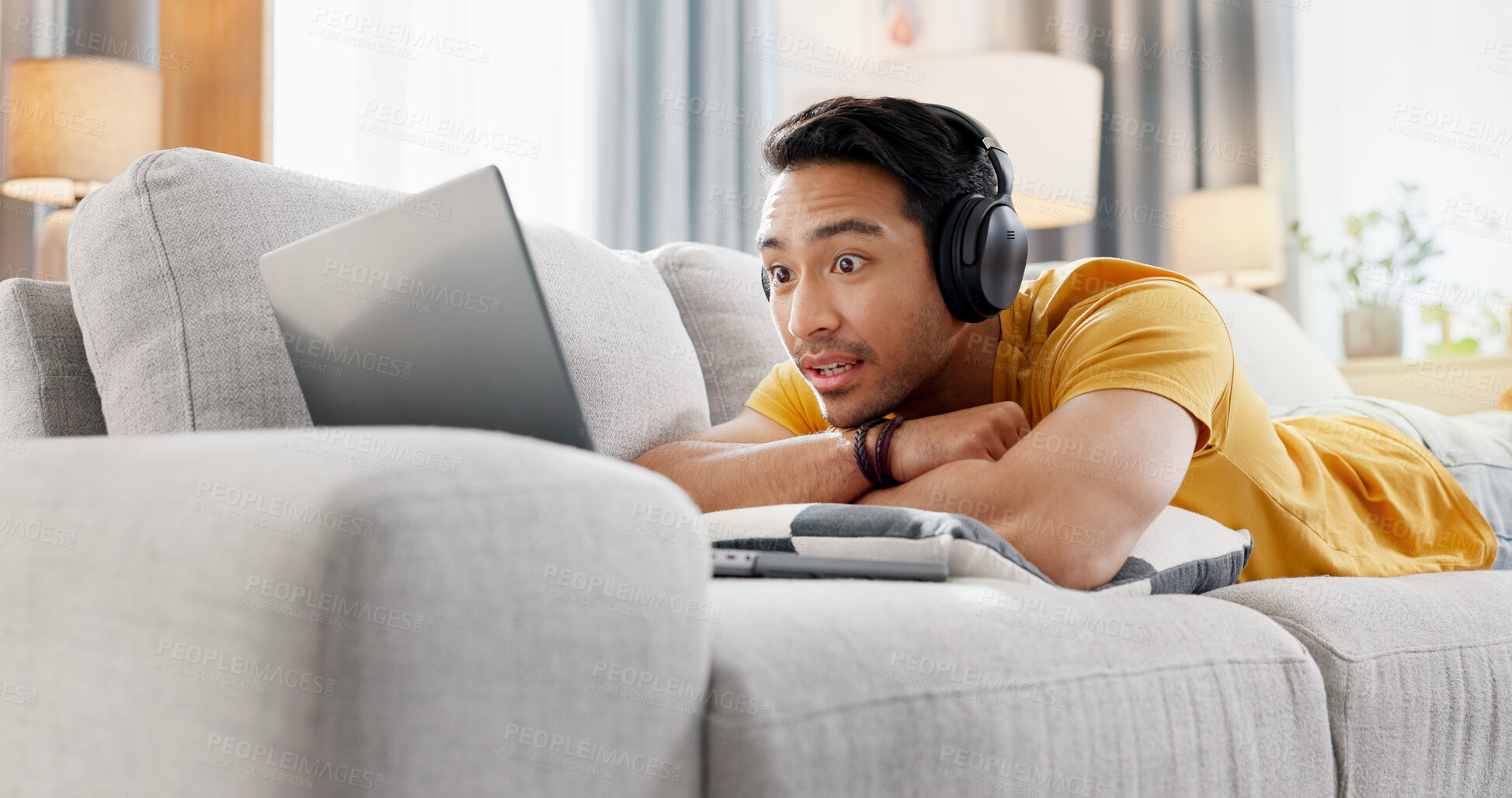 Buy stock photo Headphones, laptop and surprise with man on sofa in living room of home for online subscription. Big eyes, computer and relax with person in apartment for break, entertainment or video streaming