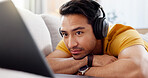 Headphones, laptop and video streaming with man on sofa in living room of home for online subscription. Computer, relax and watching movie with person in apartment for break, entertainment or media