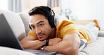Man, laptop and headphones on sofa for relax, social media and video streaming or website in home. Movie, internet audio and male person on couch with technology, break and watching film on app