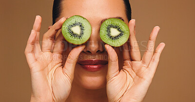 Buy stock photo Beauty, kiwi and eyes with woman in studio for vitamin c, skincare and antioxidants glow. Self care, organic dermatology and natural enzyme facial with person and fruit on brown background for detox