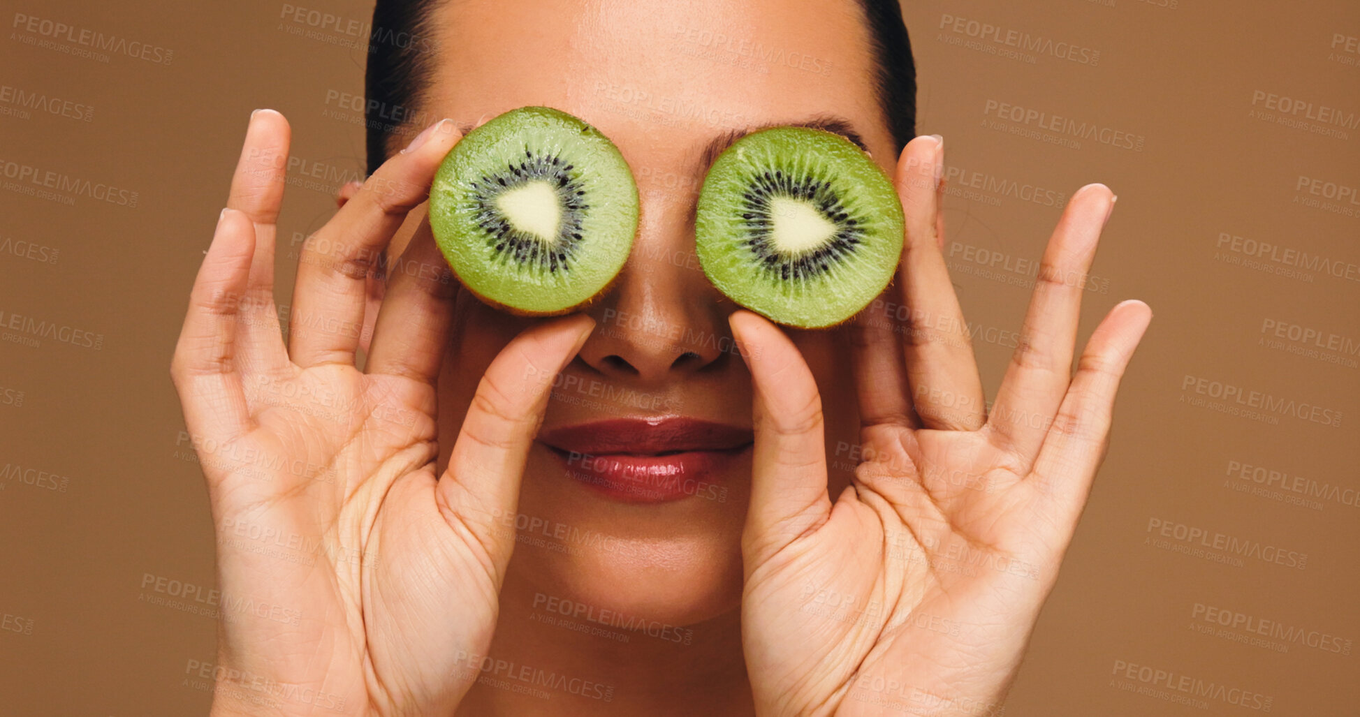 Buy stock photo Beauty, kiwi and eyes with woman in studio for vitamin c, skincare and antioxidants glow. Self care, organic dermatology and natural enzyme facial with person and fruit on brown background for detox