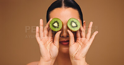 Buy stock photo Skincare, kiwi and eyes with woman in studio for vitamin c, beauty and antioxidant glow. Self care, organic dermatology and natural enzyme facial with person and fruit on brown background with space