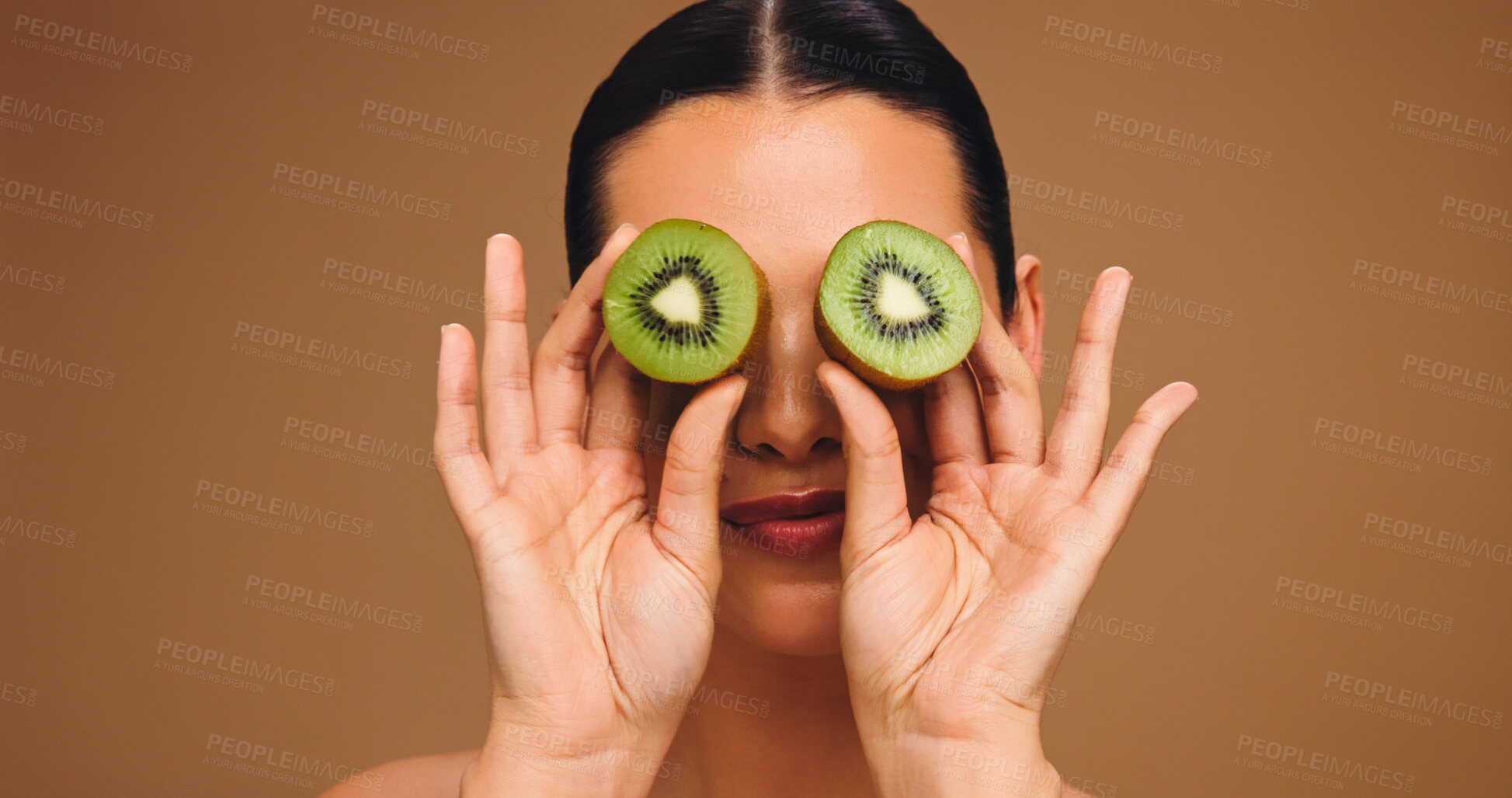 Buy stock photo Skincare, kiwi and eyes with woman in studio for vitamin c, beauty and antioxidant glow. Self care, organic dermatology and natural enzyme facial with person and fruit on brown background with space