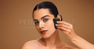 Buy stock photo Beauty, gua sha and portrait of woman in studio for lymphatic drainage, skincare and self care. Detox glow, jade tool and facial massage with person on brown background for holistic benefit and space