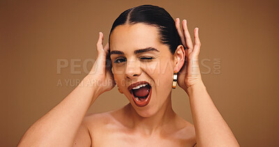 Buy stock photo Woman, beauty and wink in studio portrait with earrings, makeup and playful with funny face on background. Girl, model and cosmetics with sign, skin and mockup space with transformation in Portugal