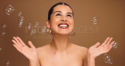 Buy stock photo Bubbles, excited and woman in studio for skincare, beauty and cosmetics for wellness, health and glow. Happy, space and person with soap for spa aesthetic, makeup and dermatology on brown background