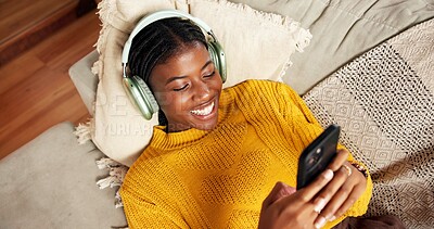 Buy stock photo Black woman, phone and relax on sofa with headphones, edit playlist and social media. Above, person and smile in home with music tech, streaming radio and audio website subscription in living room