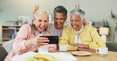 Buy stock photo Bunny ears, coffee and selfie with senior friends in dining room of home together for funny memories. Beverage, emoji and photograph with old people laughing in apartment for bonding or social media