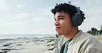 Thinking, man and relax with headphones at beach for holiday ideas, vacation music or sightseeing. Sky space, person or listening to song on promenade for weekend trip, exploring nature or reflection
