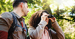 Couple, hiking and happy with binoculars in forest for sightseeing, adventure and outdoor in summer. Woman, man and interracial love for birdwatching, direction or smile with trekking in woods