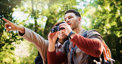 Buy stock photo Couple, hiking and point with binoculars in forest for sightseeing, adventure and outdoor in summer. Woman, man and interracial love for birdwatching, direction or smile with trekking in woods