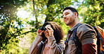 Happy couple, hiking and binoculars in forest for sightseeing, adventure and outdoor for summer. Woman, man and interracial love for birdwatching, tourist or smile for view with trekking in woods