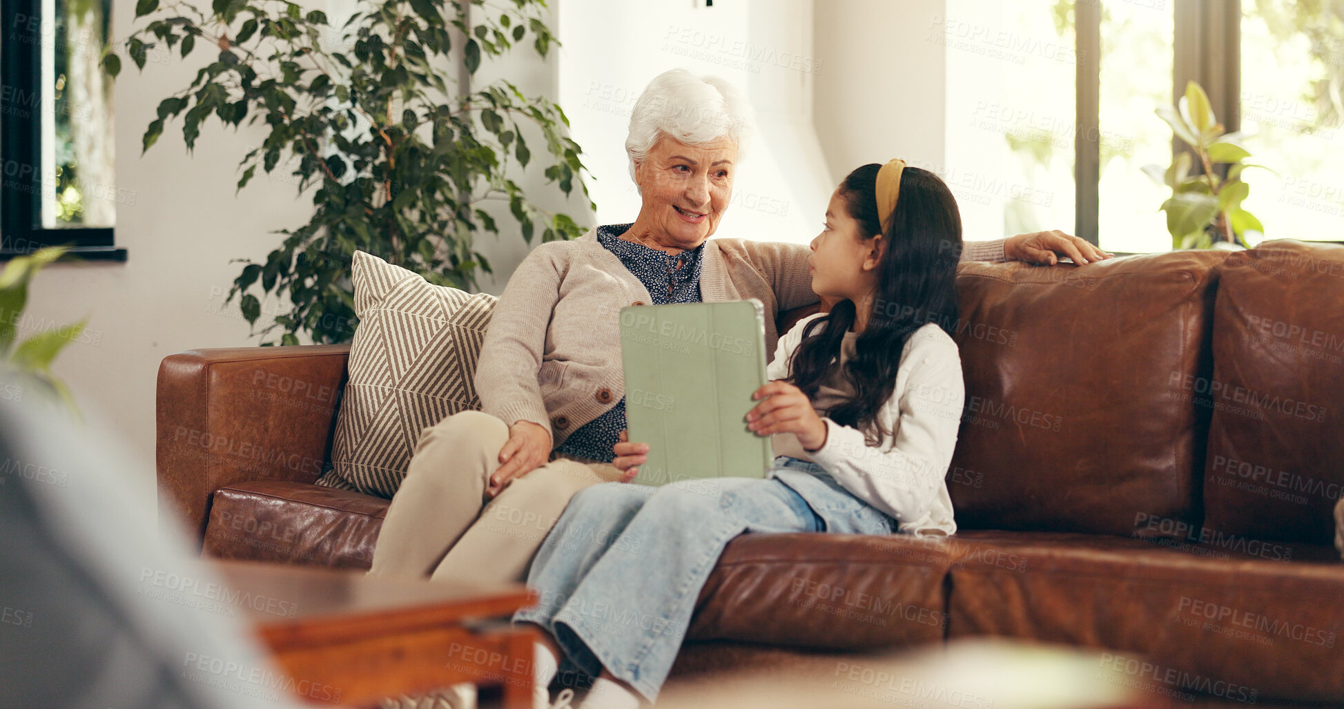 Buy stock photo Home, tablet and grandmother on sofa, girl and bonding together with education games on internet. Learning, old woman or family on couch, granny and child with tech, talking or digital app for puzzle