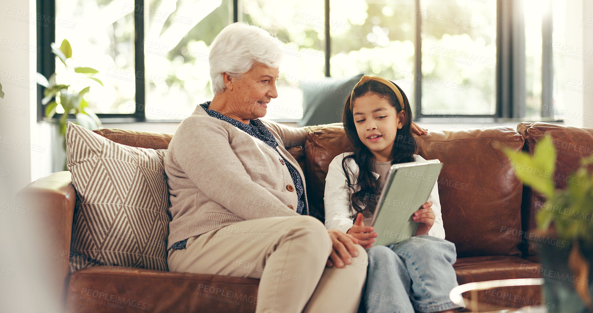 Buy stock photo Home, tablet and grandmother with girl, talking and bonding together with education games, help and tech. Learning, granny or family on sofa, child or conversation with digital app for ebook or relax