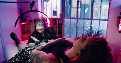 Buy stock photo Tattoo, artist and customer or women in store for permanent ink, linework design or aesthetic. Culture, self expression and tattooing parlor with people in neon studio for identity and body art