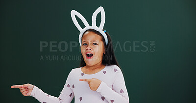 Buy stock photo Bunny ears, pointing and portrait with girl child in studio for announcement or notification. Easter, promotion and space with surprised kid isolated on green background for wow gesture or reaction