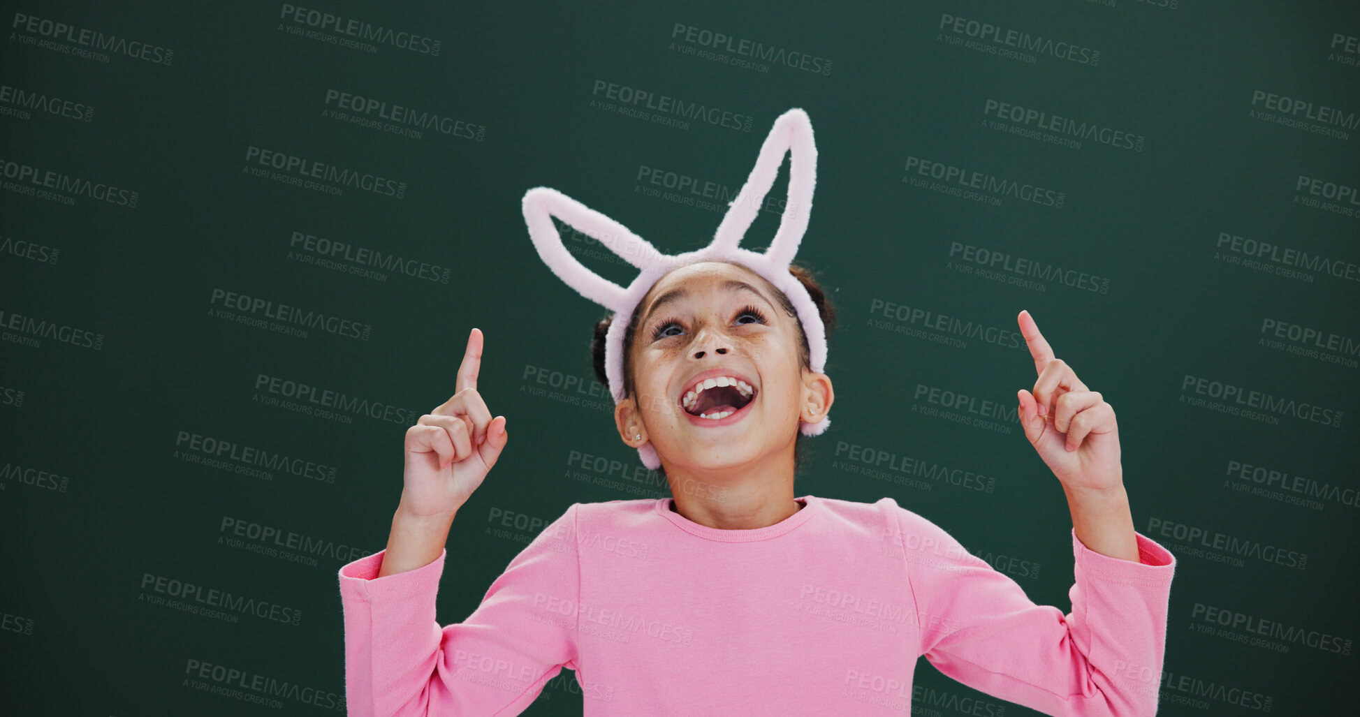 Buy stock photo Bunny ears, excited and pointing with girl child in studio for announcement or notification. Easter, promotion and surprise with happy kid isolated on green background for wow gesture or reaction