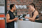 Asian man signing up for gym membership with caucasian trainer. Young coach behind reception pointing and showing where to sign. Two active and fit people standing together in health and fitness club