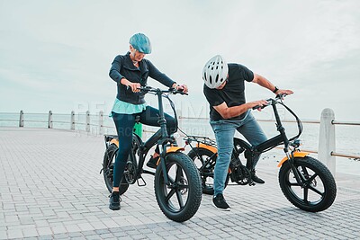 Buy stock photo Mature couple, electrical or checking bike by beach in bonding transportation, clean energy or sustainability city travel. Ebike, electricity or eco friendly bicycle for elderly man or cycling woman