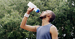 Runner, man and drink water in nature for health, wellness or exercise break. Bottle, person and thirsty athlete with  hydration liquid outdoor for workout recovery, fitness and sports nutrition