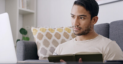 Buy stock photo Asian man, laptop and reading with book in home for journalism, remote work or research. Male person, journalist or freelancer checking notes with computer, notebook or diary for schedule or tasks