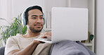 Man, laptop and relax with headphones on sofa, typing and search for movies, streaming or video at home. Person, computer and audio for smile, subscription and film on couch in lounge at apartment