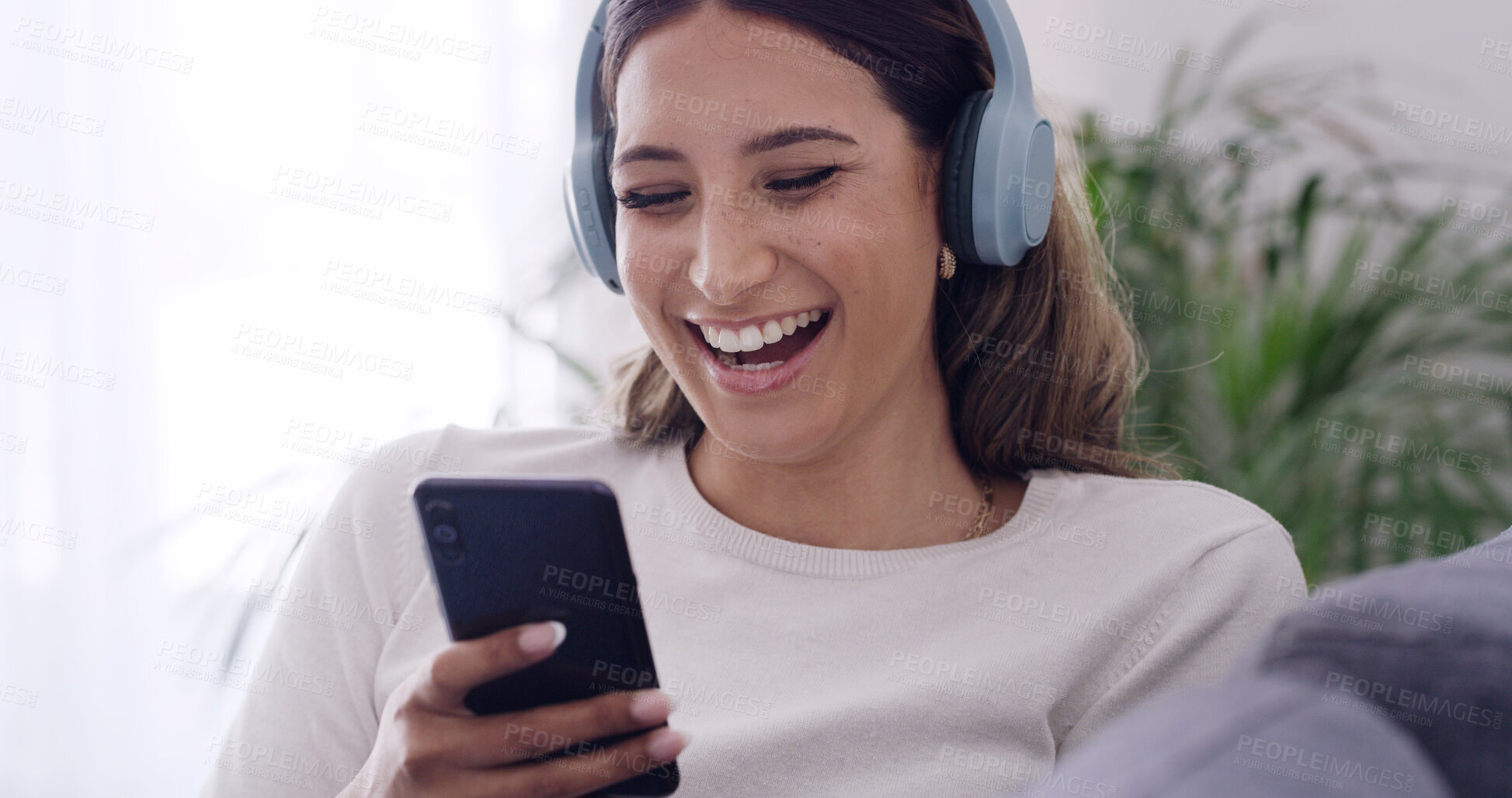 Buy stock photo Phone, laugh and woman with headphones in home, streaming service or funny video on internet. Mobile, music and happy person in living room for meme, online audio and listening to comedy podcast