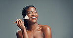 Makeup, beauty and black woman laugh with brush in studio for shine, foundation or glow. Funny, apply cosmetics and model with product for facial makeover, change and powder on gray background space