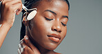 Face roller, black woman or massage in studio with skincare for beauty, dermatology or facial tension. Person, cosmetic and rose quartz tool for grooming, wellness or mockup space on gray background.