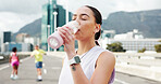 Woman, fitness and drinking with water bottle in city for workout break, rest or recovery. Active, female person or runner with mineral liquid, aqua or beverage for sports hydration in an urban town