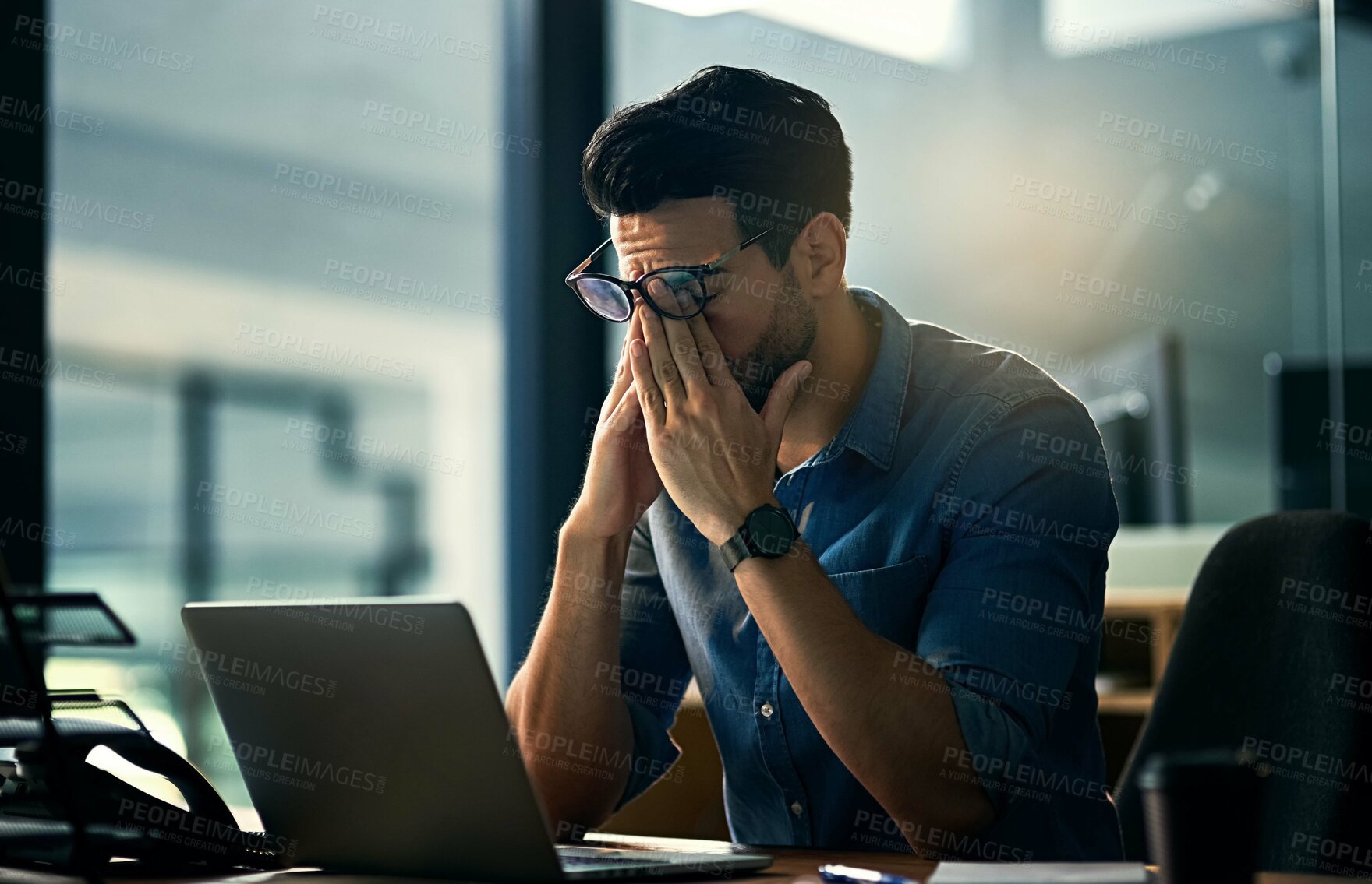Buy stock photo Shot of a young businessman experiencing stress during a late night at work